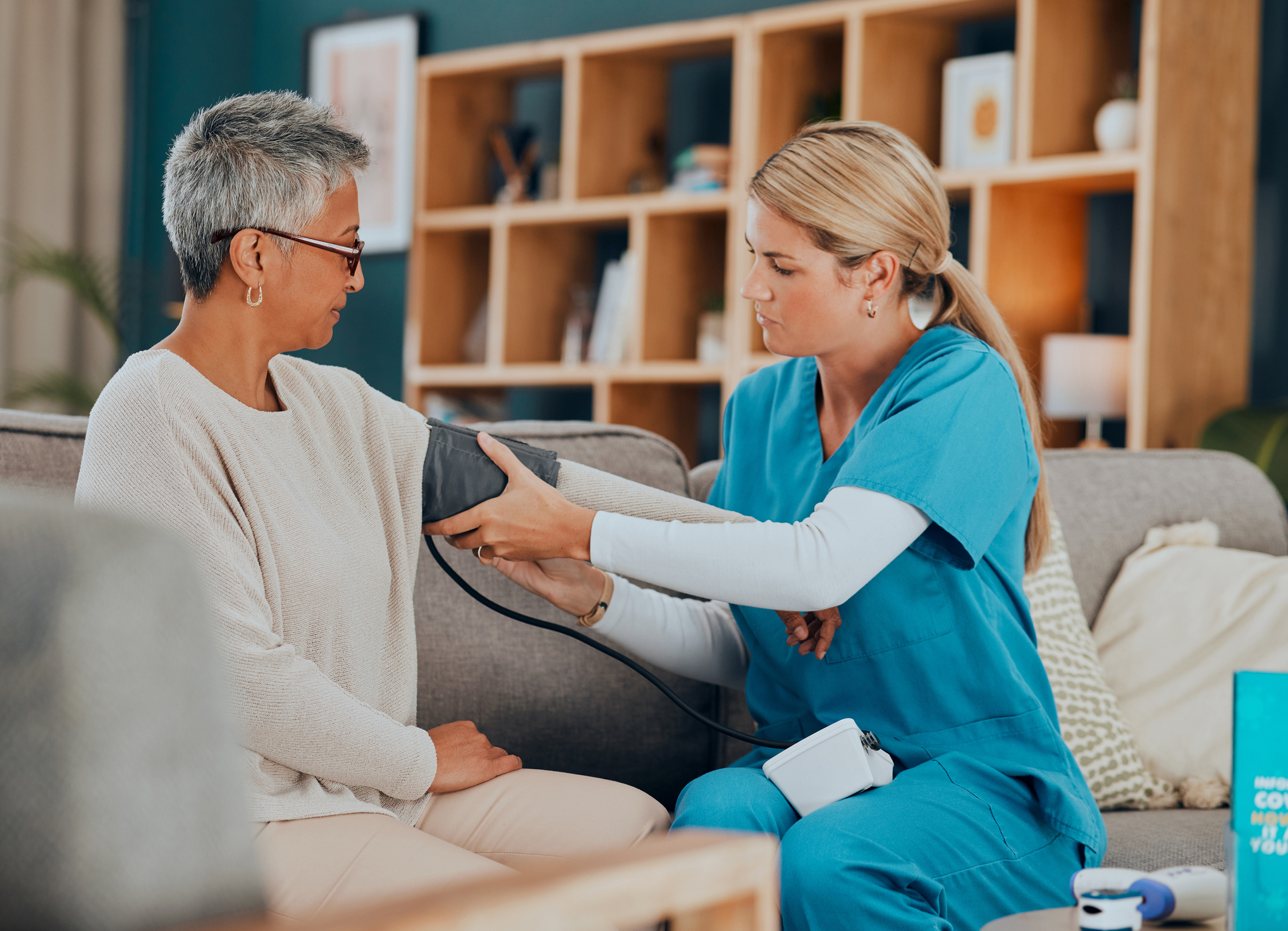 practical nurse in green scrubs taking blood pressure of older woman
