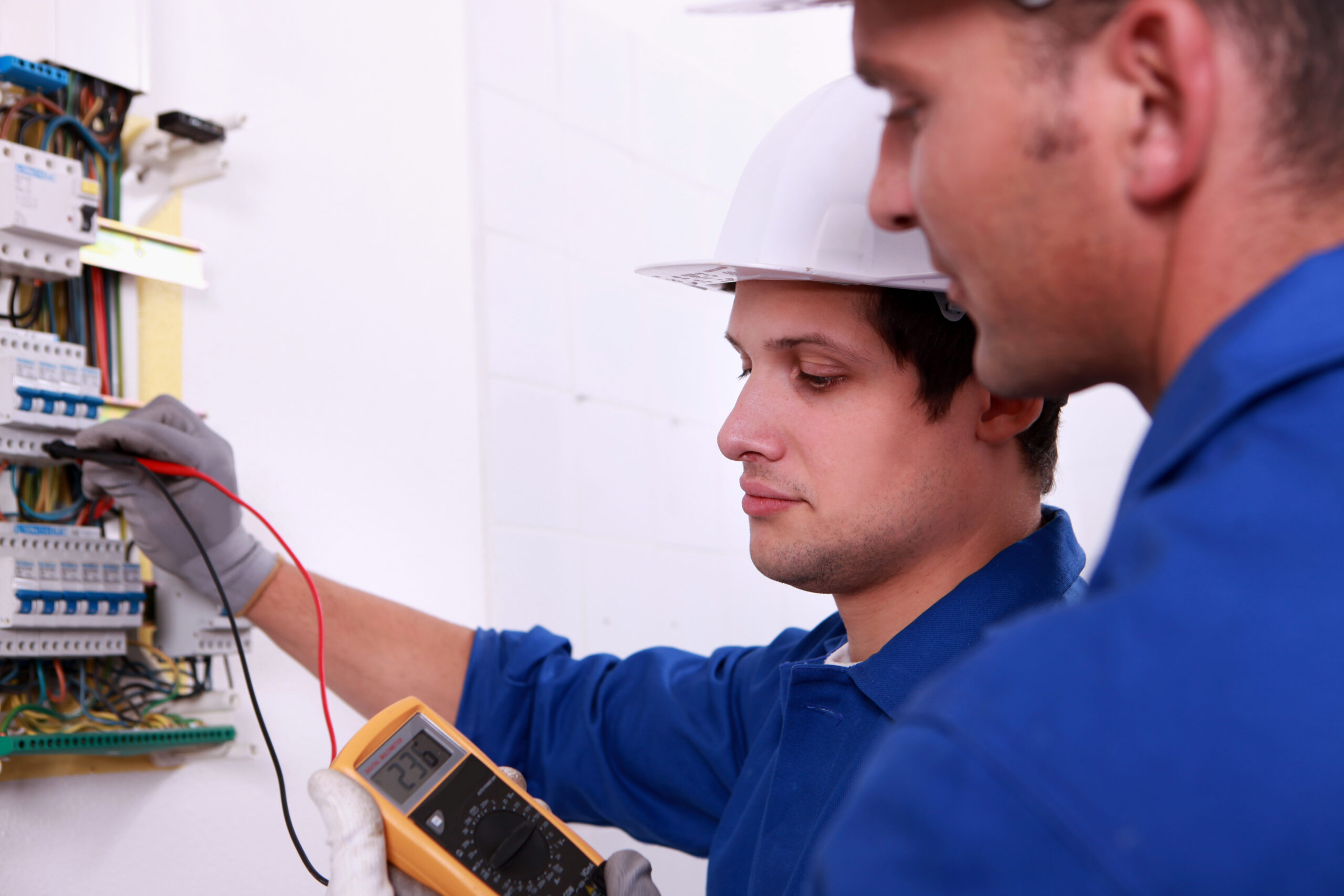 Two men in blue work clothes testing fuse box